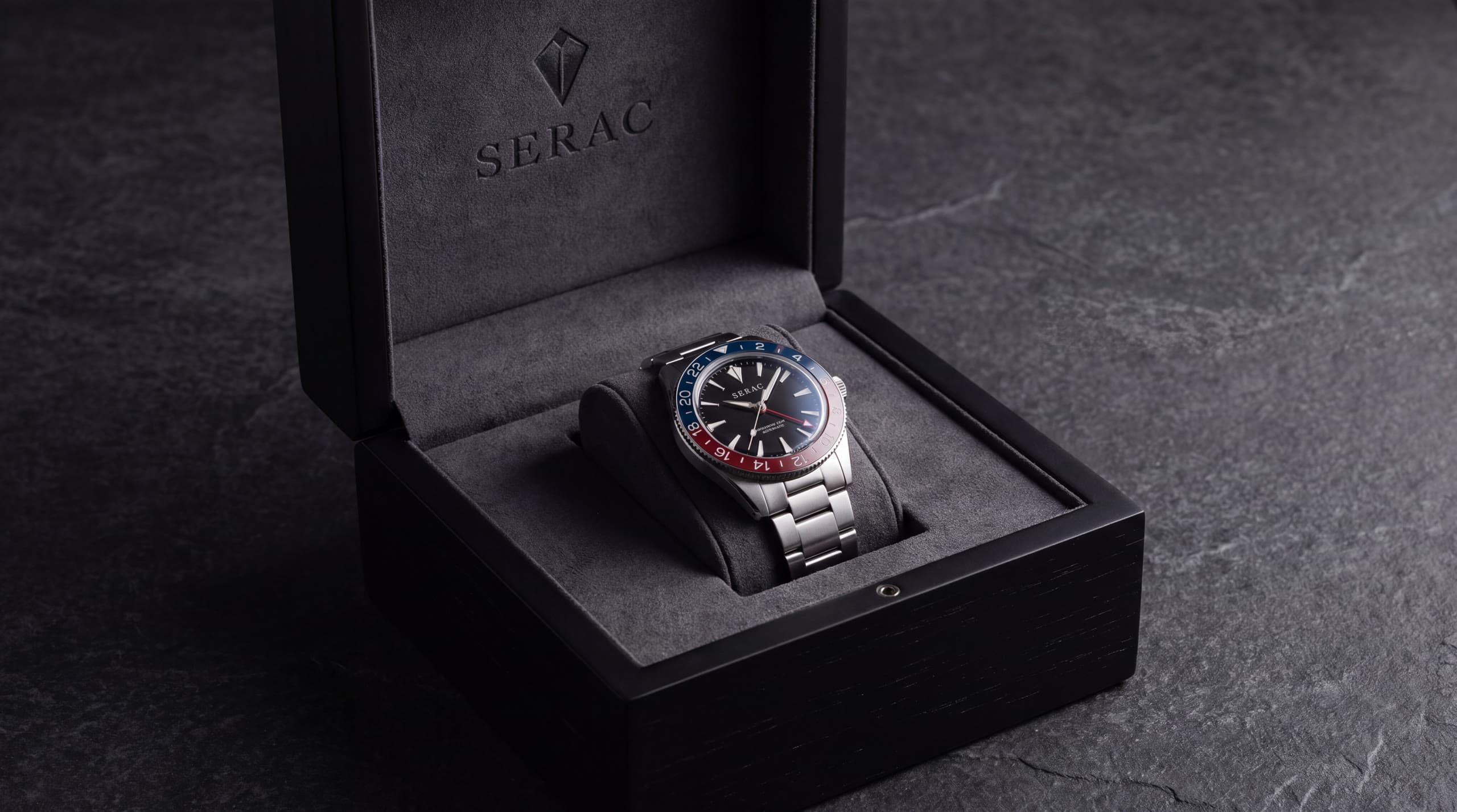 The Traverse GMT resting on its bracelet inside an open black lacquered presentation case, the SERAC peak on the lid.