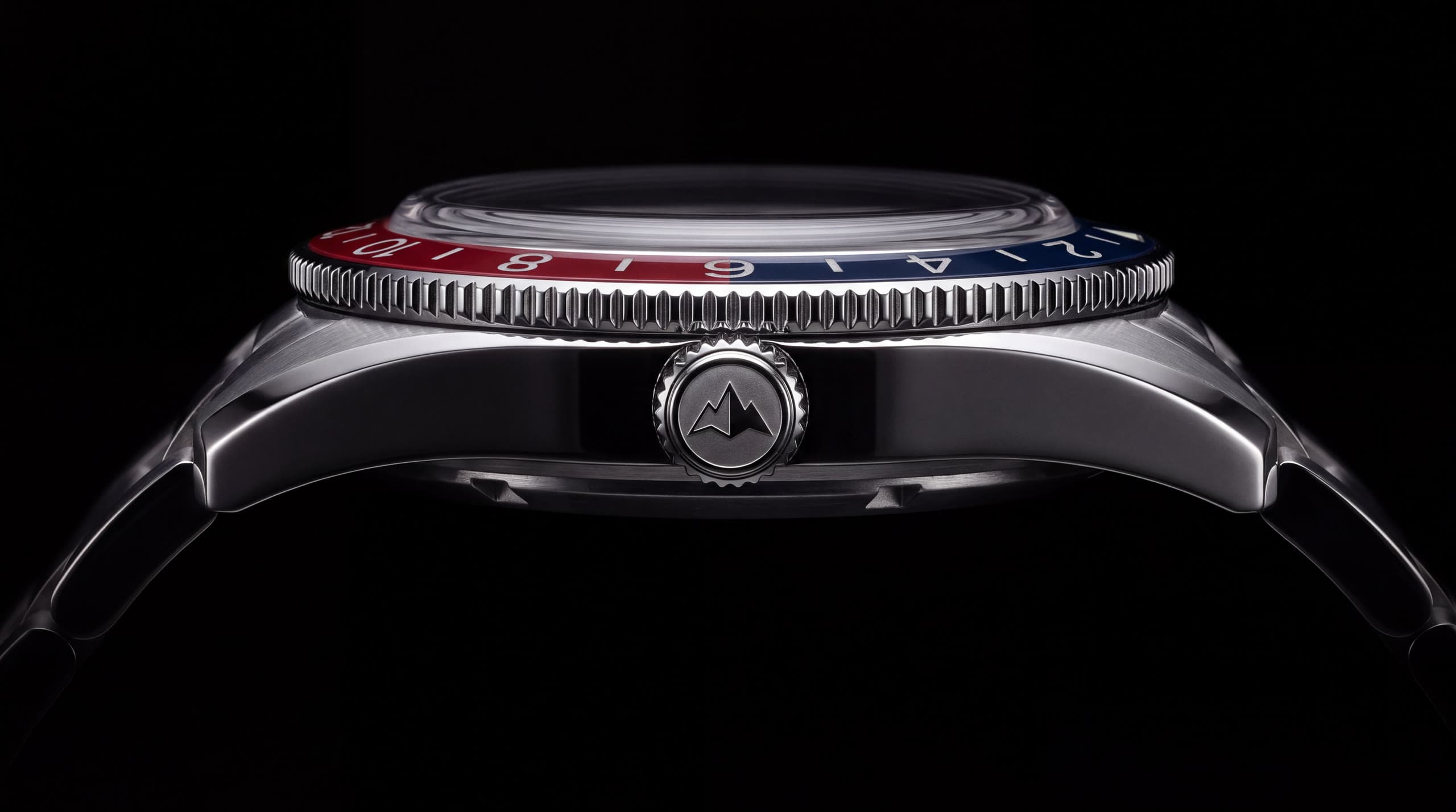 The case in profile: knurled bezel edge over the red and blue insert, polished flank and the screw-down crown engraved with the double peak.